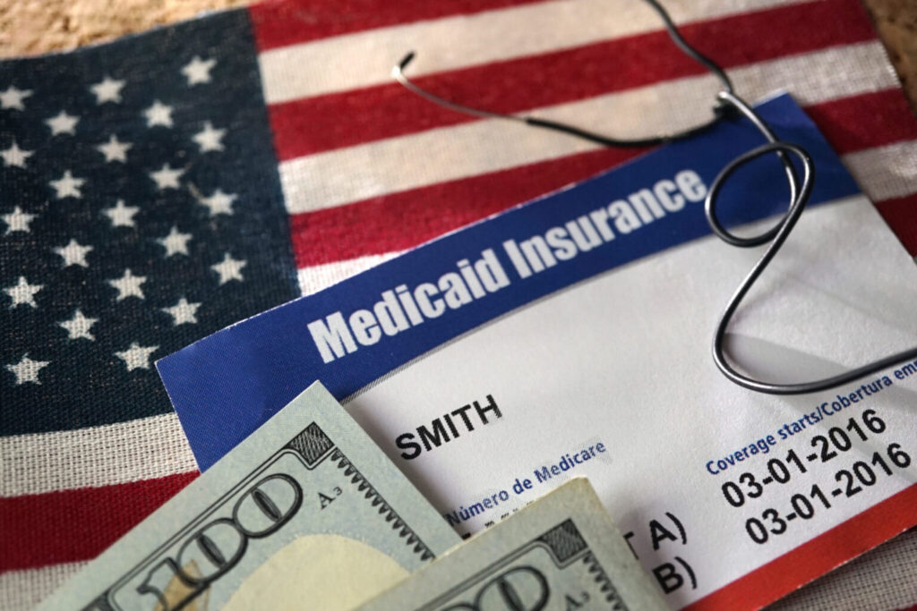U.S. flag background with a Medicaid card and $100 bills on top, illustrating the financial aspects of Medicaid in American dental care.