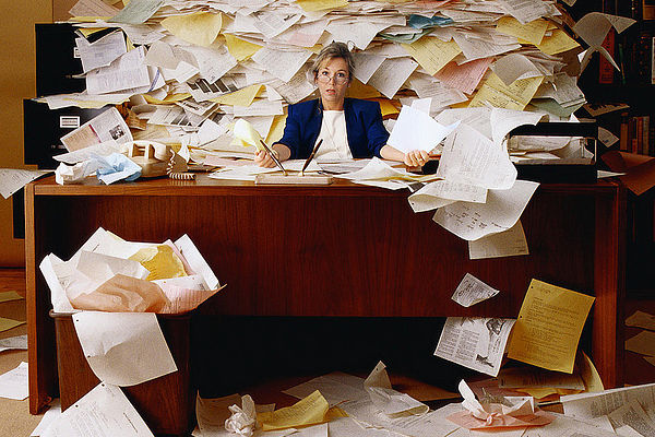 Office worker overwhelmed with a mountain of paperwork related to Medicaid dental policies.